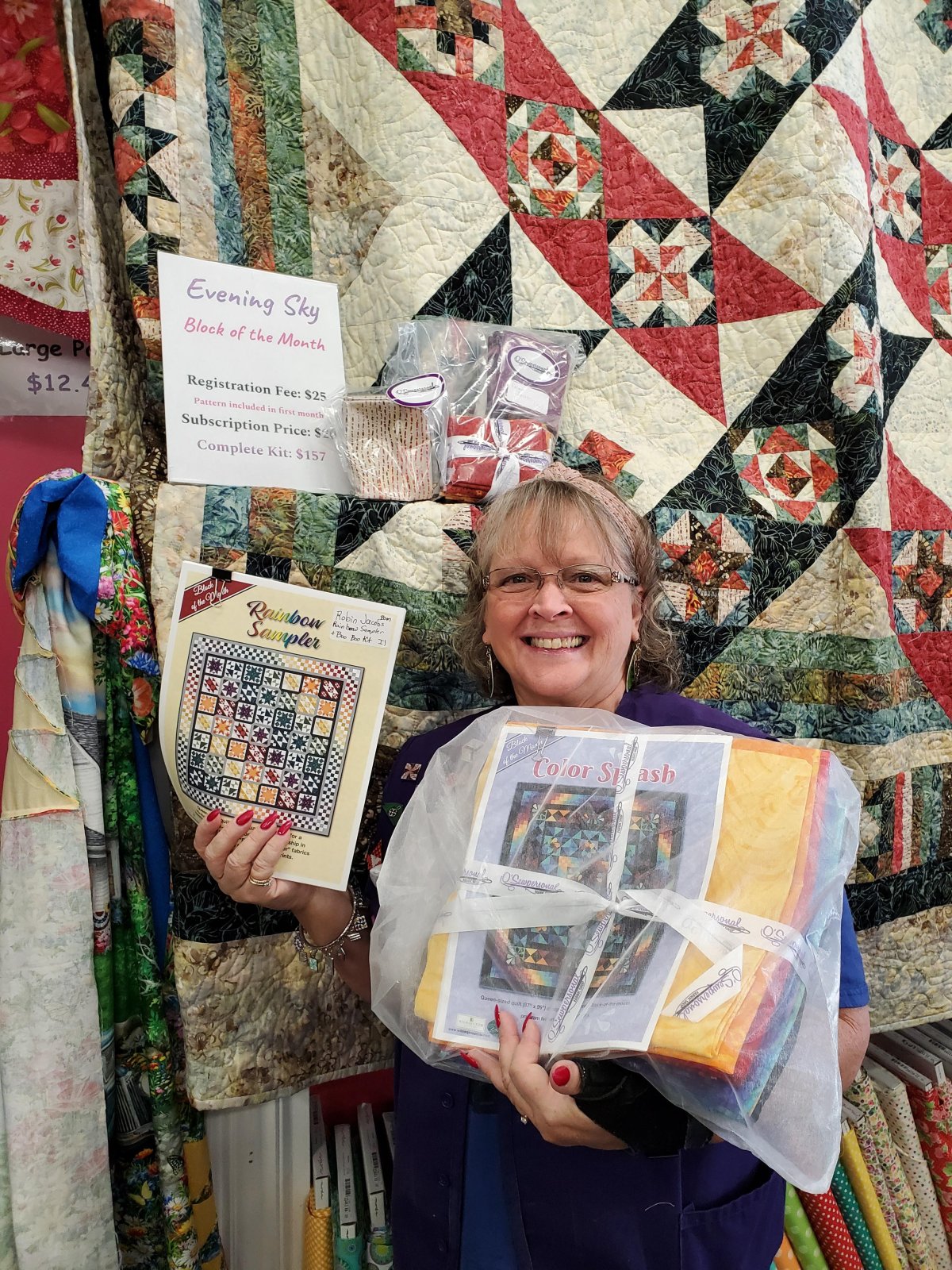 Woman standing in front of handmade quilt holding quilting patterns.