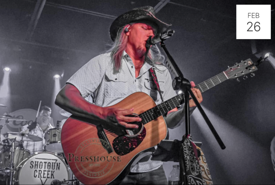 Photo of Jeremy Drake of Shotgun Creek playing acoustic guitar with drummer in background